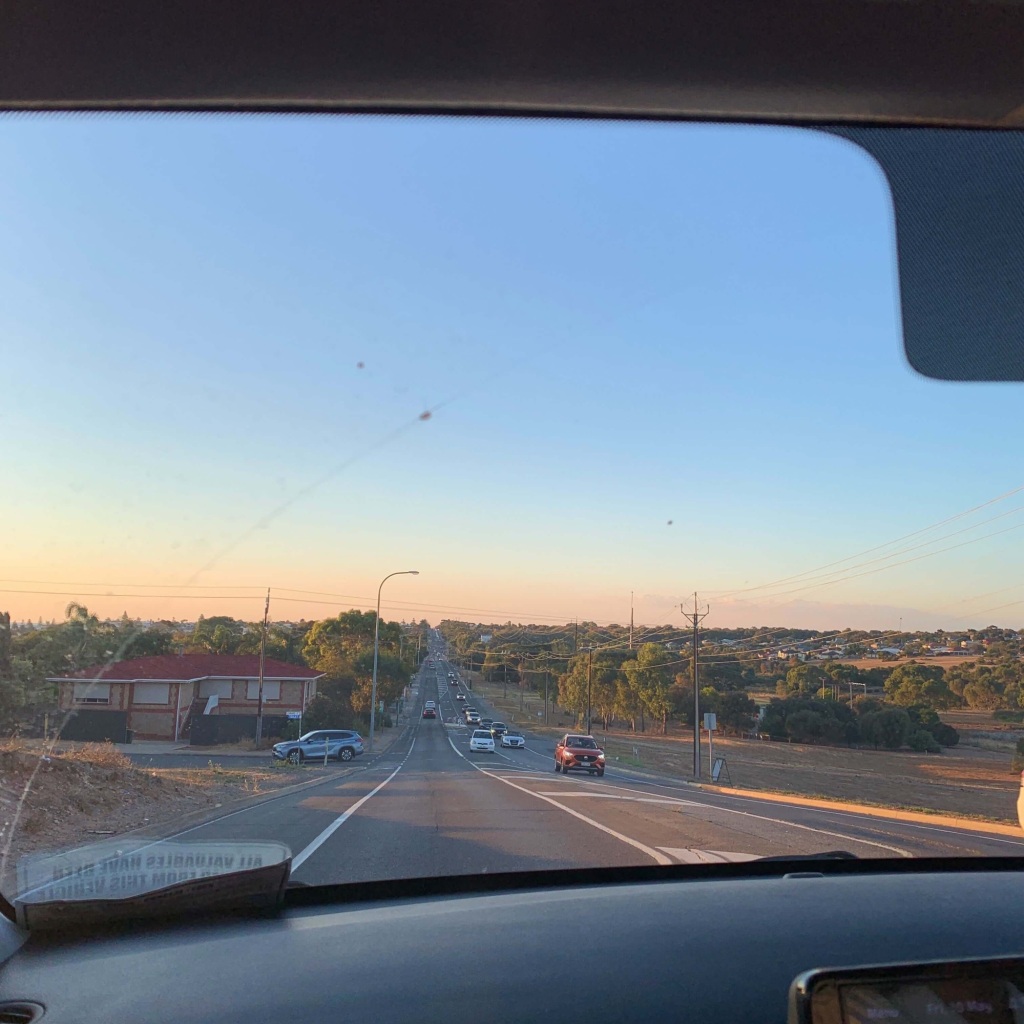 Photo of a main road with sunset in the horizon ahead, taken from the front passenger seat of a car. 